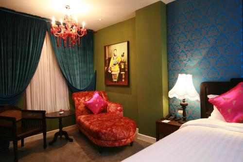 a bedroom with a bed and a chair and a chandelier at Shanghai Mansion Bangkok in Bangkok