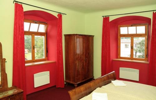 a bedroom with red curtains and a bed and a cabinet at Penzion Haberský vrch in Habří