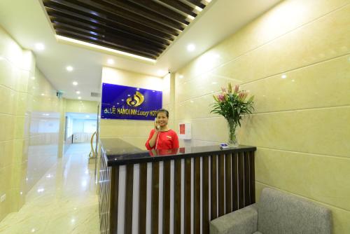 a woman standing at a counter in a lobby at Blue Hanoi Inn Luxury Hotel in Hanoi