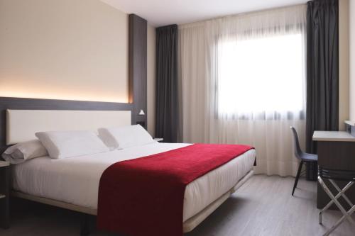 a bedroom with a bed with a red blanket and a window at Hotel New Bilbao Airport in Derio
