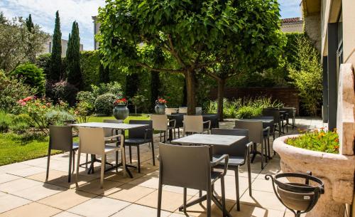 a patio with tables and chairs in a garden at Avignon Grand Hotel in Avignon
