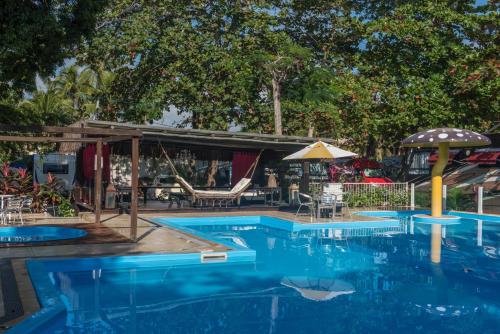 a swimming pool with an umbrella and tables and chairs at Hotel Mundaí Praia Camping e Est para Mh in Porto Seguro