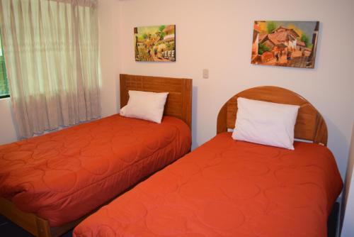 2 camas en una habitación con sábanas de color naranja en Kuski Hospedaje, en Cusco