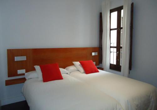 2 weiße Betten mit roten Kissen im Schlafzimmer in der Unterkunft Apartamentos Turísticos Mauror in Granada