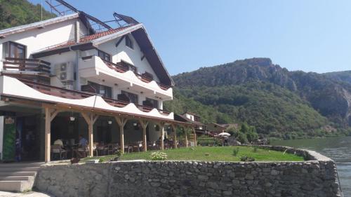 a building next to a body of water with mountains at Pensiunea Cazanele Dunarii in Dubova