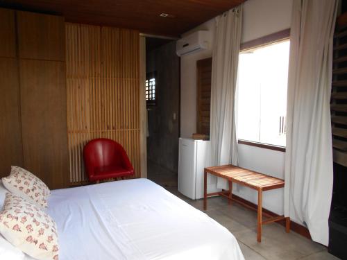 a bedroom with a white bed and a red chair at Hotel Villaggio Tudo Bom in Uruau