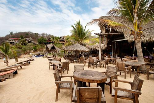 a beach with many tables and chairs and palm trees at El Alquimista Yoga Spa in Zipolite