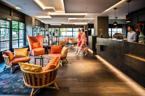 a lobby with orange chairs and a woman walking a dog at SAKS Urban Design Hotel Frankfurt in Frankfurt