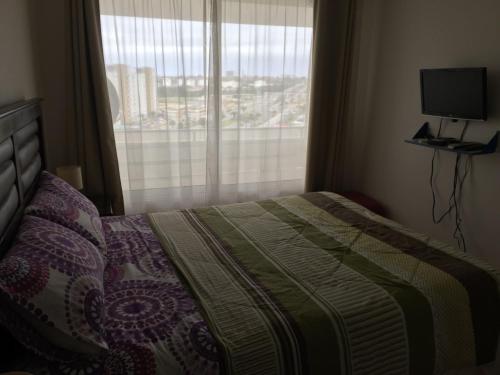 a bedroom with a bed and a window with a television at Pronejoet Departamentos La Herradura in Coquimbo