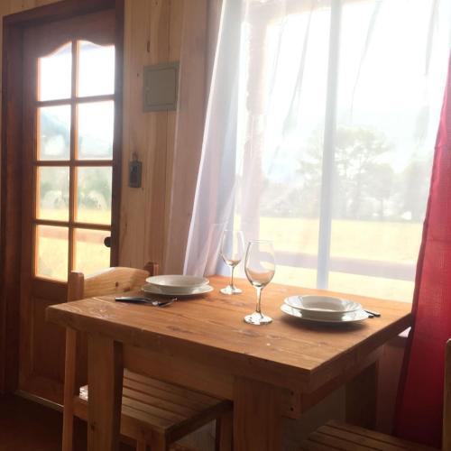 a wooden table with two glasses and plates on it at Cabañas Los Canelos Pucon, Hermosa Granja de 20 hectaréas a orillas del Río Liucura in Pucón