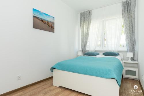 a white bedroom with a bed and a window at Jantar Apartamenty - Pod Lipami in Kołobrzeg