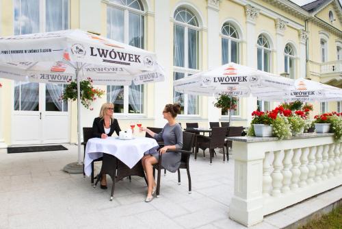 dos mujeres sentadas en una mesa bajo sombrillas en Uzdrowisko Cieplice - Jelenia Góra - Pawilon Edward, en Jelenia Góra