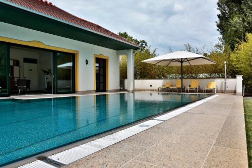 a swimming pool with an umbrella next to a house at Hubertus Hof Landhotel in Balatonfenyves