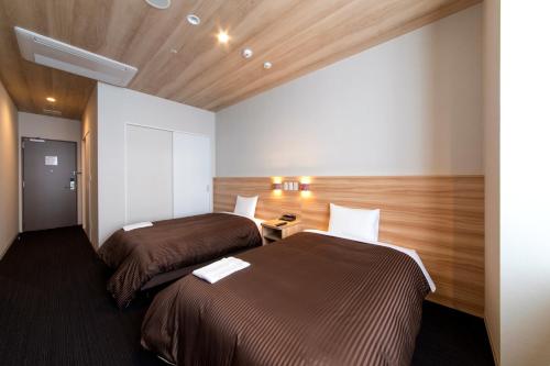 two beds in a room with wooden floors and ceilings at Izumisano Center Hotel Kansai International Airport in Izumi-Sano