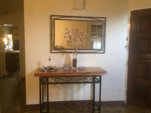 una mesa con un espejo y un jarrón con flores. en The Bedford View Guest House, en Germiston