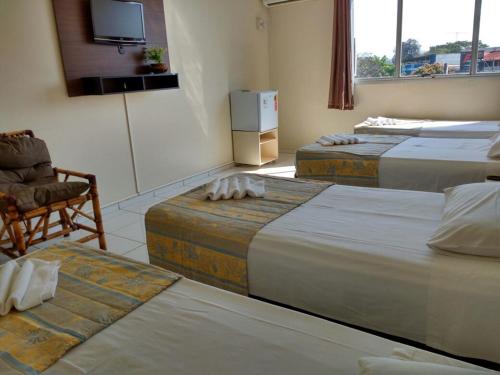 Habitación con 3 camas, silla y TV. en Alvorada Iguassu Hotel, en Foz do Iguaçu