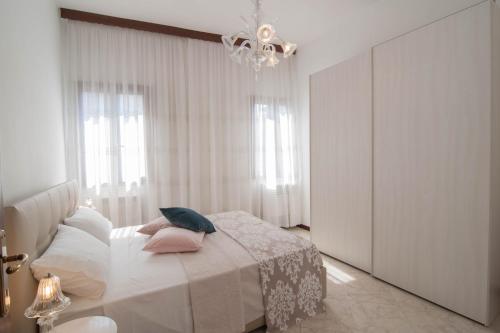 biała sypialnia z łóżkiem z poduszkami i żyrandolem w obiekcie Riva Excelsior Apartment w Wenecji
