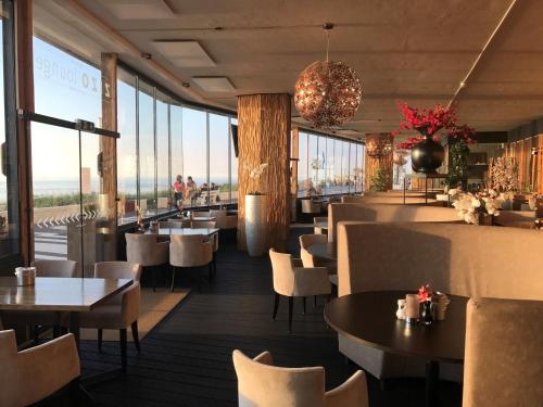 a dining room with tables and chairs and windows at Palace Hotel Zandvoort in Zandvoort