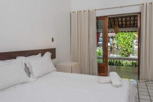 um quarto com uma cama branca e uma porta de vidro deslizante em Hotel Mundaí Praia Camping e Est para Mh em Porto Seguro