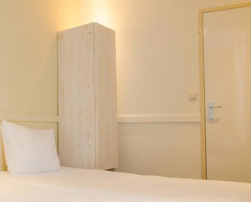 a bed with a wooden cabinet and a white pillow at City2Beach Hotel in Vlissingen