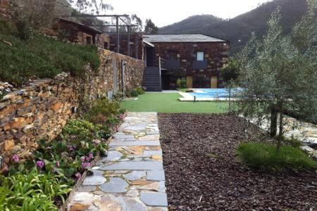 a garden with a stone wall and a swimming pool at Passadiço Art and River House in Paradinha