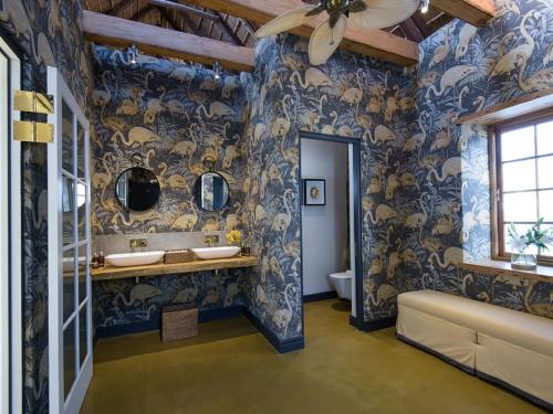 een badkamer met 2 wastafels en blauw en goud behang bij The Old Rectory in Plettenbergbaai