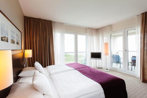 a bedroom with a large white bed and a balcony at A-ROSA Sylt in List