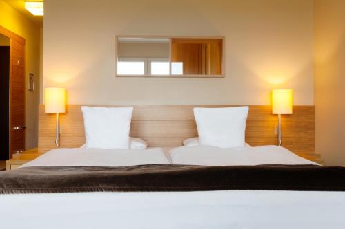 a bedroom with two white beds with two lamps at A-ROSA Sylt in List