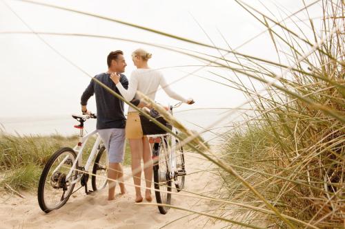 a man and a woman standing next to a bike on the beach at A-ROSA Sylt in List