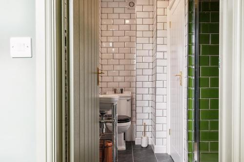 a bathroom with a white toilet and green tiles at The Coach House in Derby