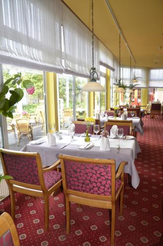 a restaurant with white tables and chairs and windows at Hotel Landhaus Dierkow in Rostock