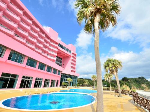 a pink building with a swimming pool and palm trees at Tanegashima Iwasaki Hotel in Minamitane