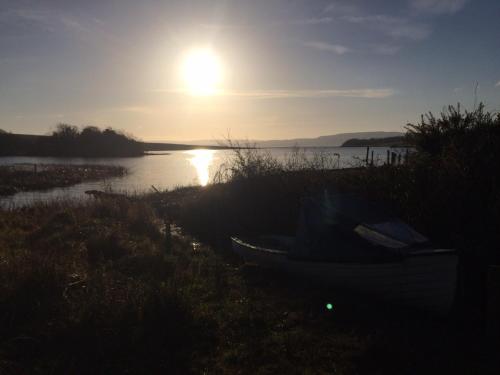 a boat sitting on the shore of a lake at sunset at Erinona Chalet in Kesh