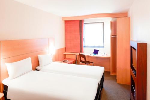 a hotel room with two beds and a desk with a laptop at ibis London Elstree Borehamwood in Borehamwood