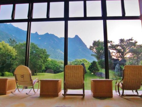 a room with three chairs and a large window at Yakushima Iwasaki Hotel in Yakushima