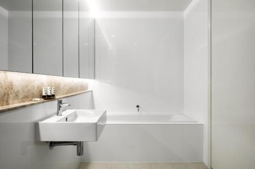 a white bathroom with a sink and a bath tub at Knightsbridge Canberra in Canberra