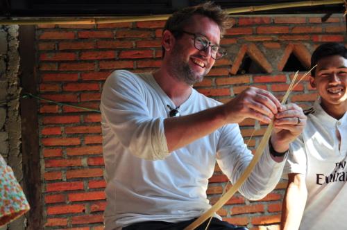 a man with glasses playing with a wooden bow at Mu Homestay in Tetebatu