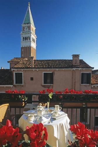a table with red flowers and a clock tower at San Marco Palace in Venice