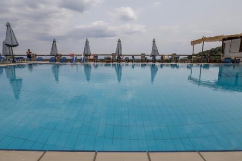 a large blue swimming pool with tables and umbrellas at Pilio Sea Horizon Hotel in Tsagarada