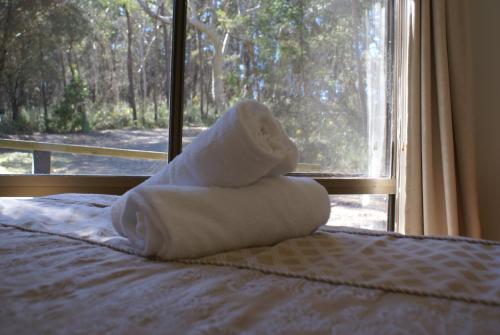 a pile of towels sitting on a bed with a window at Twin Falls Bush Cottages in Fitzroy Falls