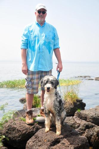 a man standing on rocks with a dog on a leash at Victoria Lake View Guesthouse & Safaris in Entebbe