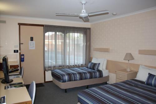 a hotel room with two beds and a desk at Raglan Motor Inn in Warrnambool