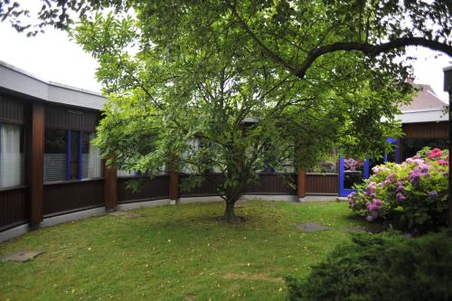 a tree in the yard of a building with flowers at Hôtel Agena in Faches-Thumesnil