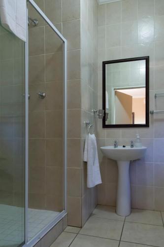 a bathroom with a shower and a sink and a mirror at Bayswater Lodge in Bloemfontein
