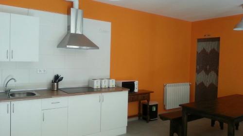 a kitchen with white cabinets and an orange wall at Albergue Orion in Castrojeriz