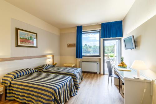 a bedroom with two beds and a desk and a window at Hotel Country Club in Capannori