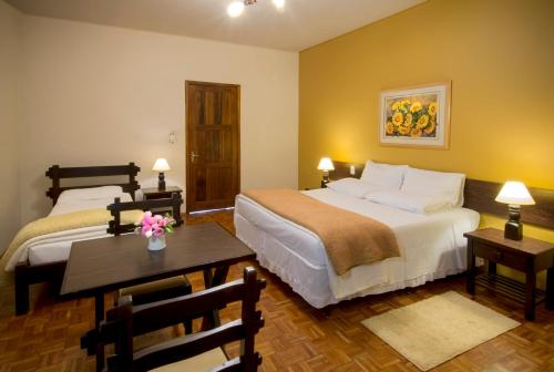 a hotel room with two beds and a table with flowers on it at Hotel Jardim Europa in Ijuí