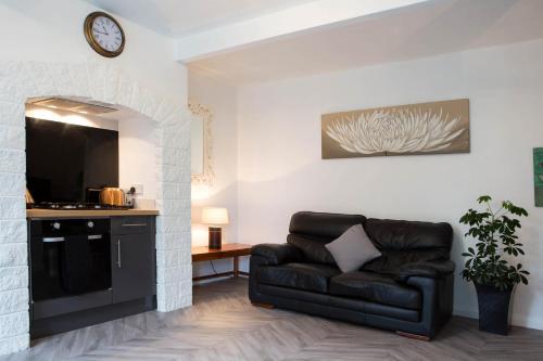 a living room with a black leather couch and a tv at The Retreat at Plover Cottage Lindley in Huddersfield
