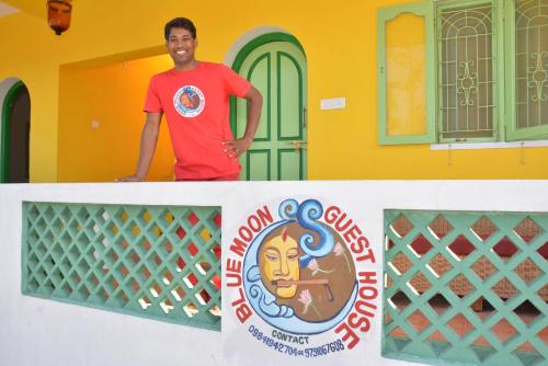 a man standing on top of a wall with a sign at Blue Moon Guest House in Mahabalipuram