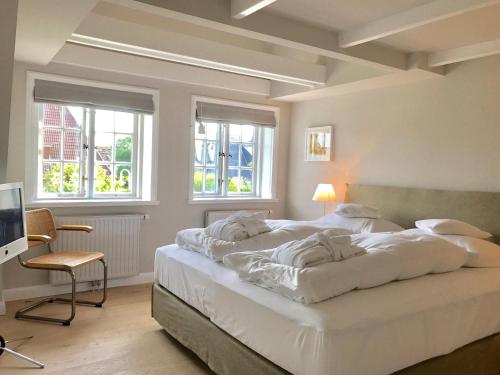 a bedroom with a large white bed and windows at Kleiner Ulenhof in Wenningstedt